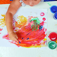 Young child finger-painting with colored paint on a poster in a learning center.